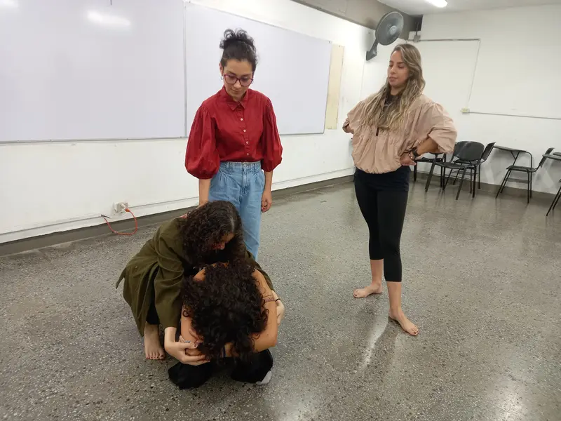 Dos integrantes de pie observan a una pareja que se abraza en el piso durante una escena