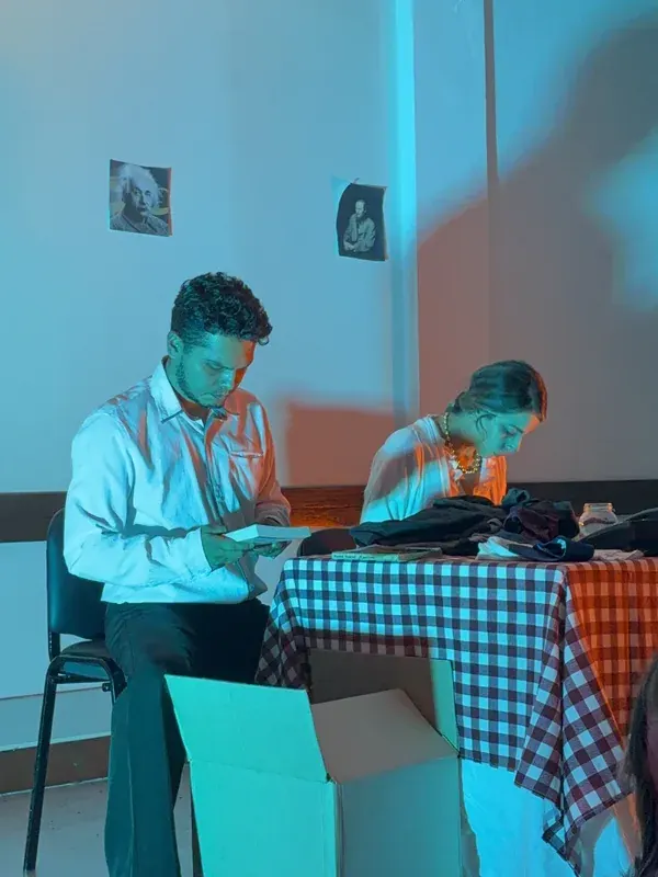 Los intérpretes de La autopsia, sentados a la mesa de mantel a cuadros bajo luz azul, durante el debut