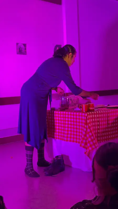 Una actriz en escena bajo luz magenta, junto a una mesa con mantel a cuadros, el día del debut