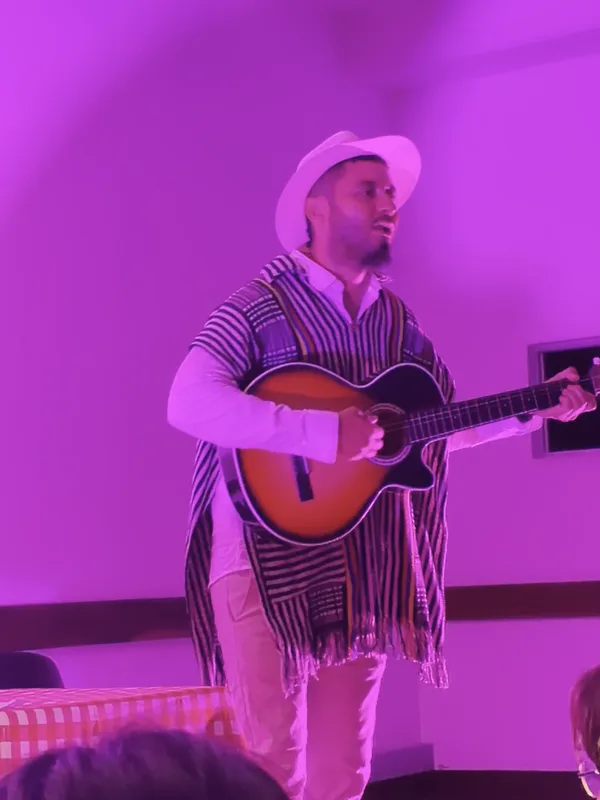 Un músico con sombrero y poncho toca la guitarra bajo luz magenta durante el debut