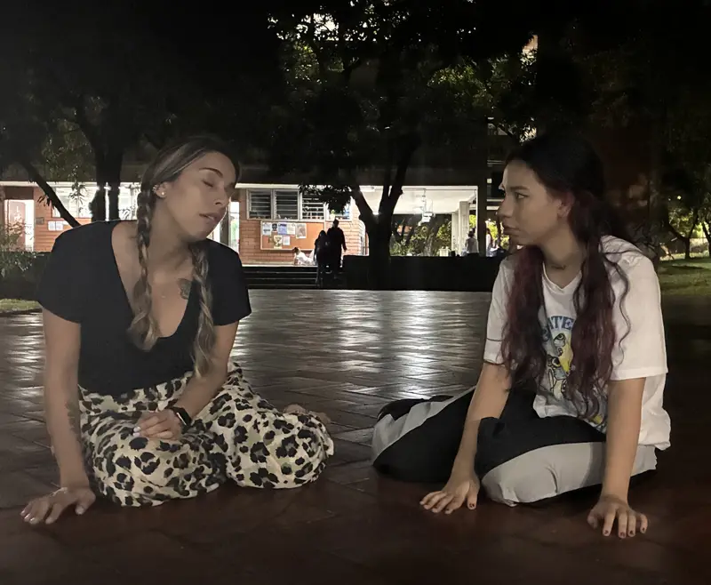 Dos integrantes sentadas en el suelo de la plaza, de noche