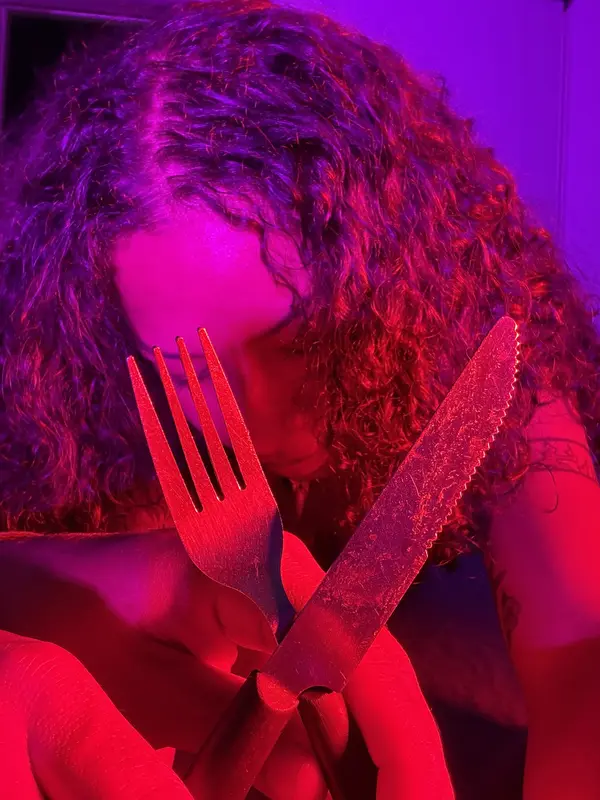 La actriz de La tortura bajo luz roja, con un tenedor y un cuchillo cruzados frente al rostro